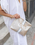 Woman in white dress holding shimmer beige with love and stripes patterned zipper pouch
