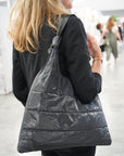 Woman holding a shimmer black puffer tote purse over shoulder
