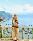 Woman standing in front of ocean and mountains in Italy with shimmer bronze shoulder purse