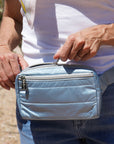 Woman unzipping a shimmer ice blue puffer crossbody fanny pack belt bag with silver zippers