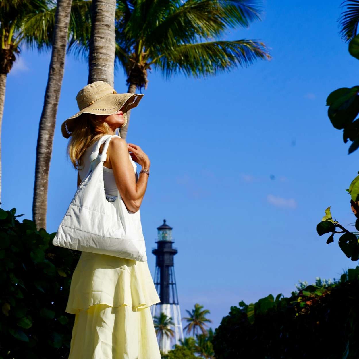 Woman wearing yellow skirt and sunhat carrying white tote bag