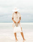 Woman in standing on ocean shoreline holding shimmer white puffer tote in front of her