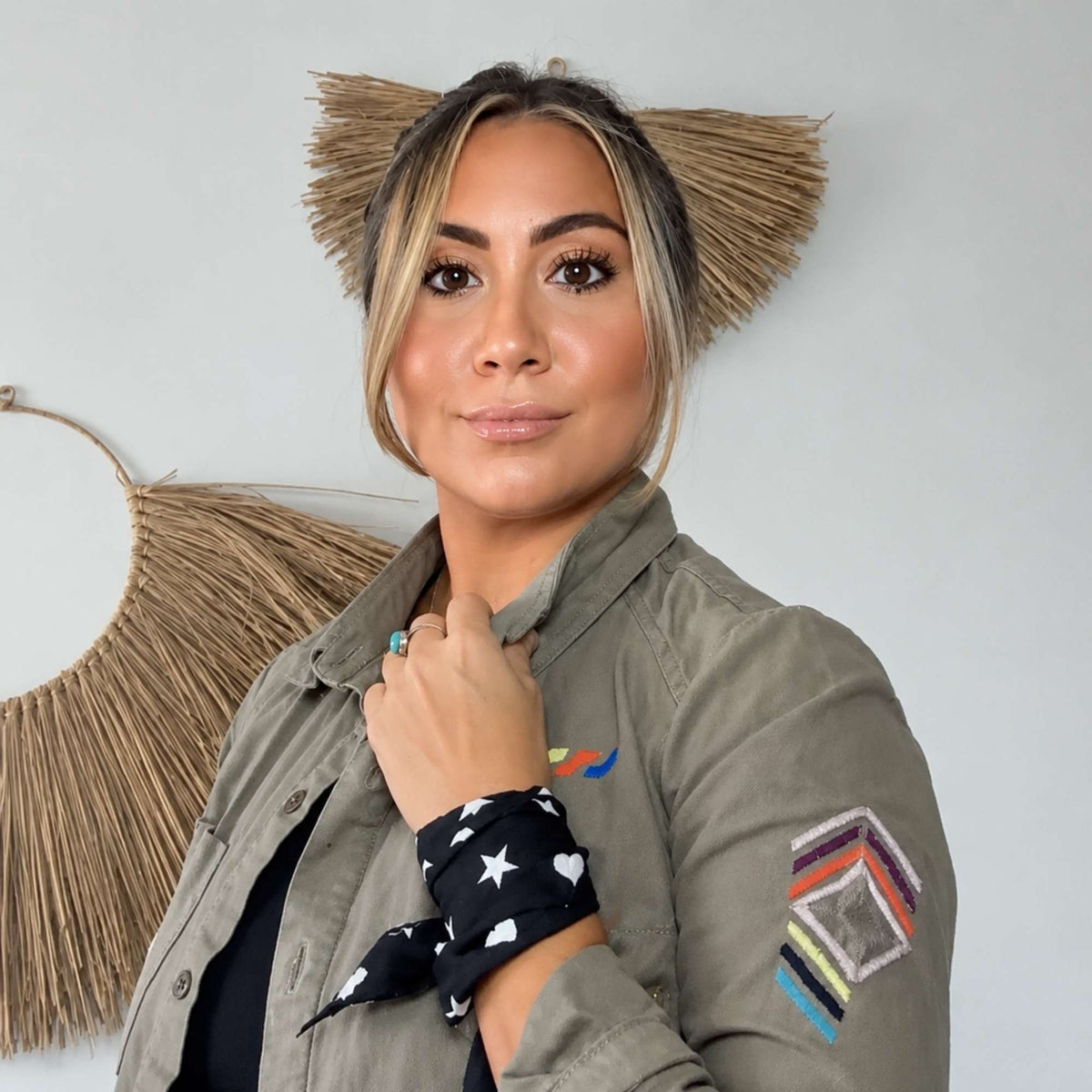 woman wearing the black Signature scarfette with white hearts, moons and stars tied around her wrist with a jacket.