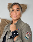 woman wearing the black Signature scarfette with white hearts, moons and stars tied around her wrist with a jacket.