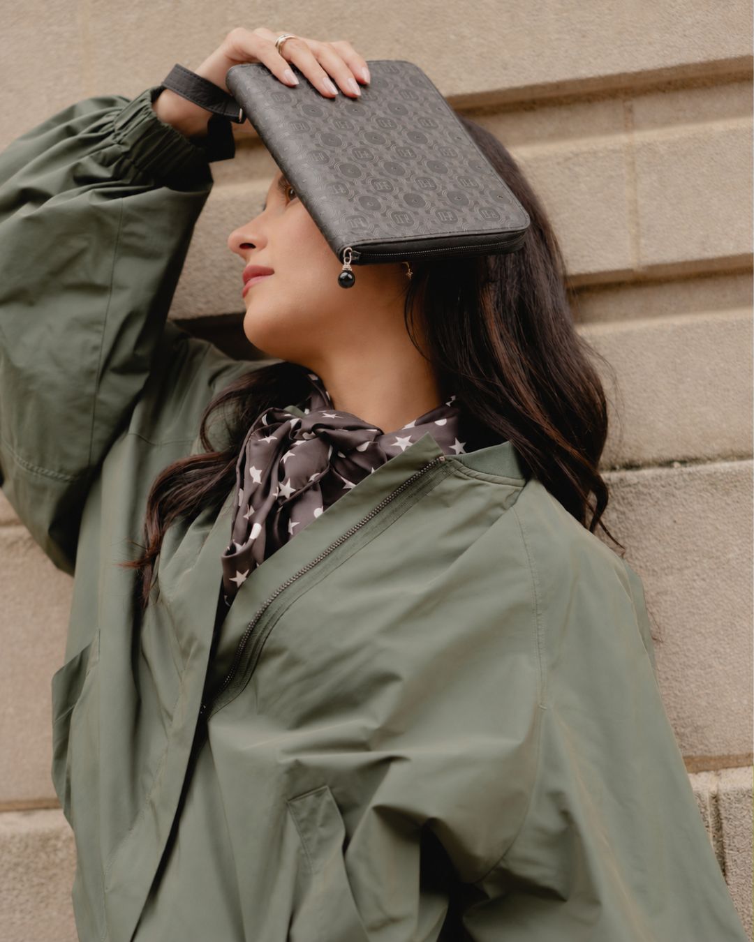 women leaning against the wall holding a black printed jewelry case.