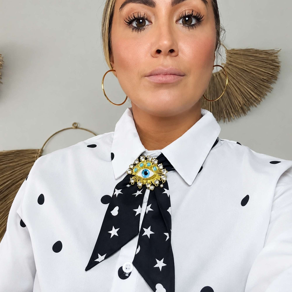 Model wearing the black Signature scarfette with white hearts, moons and stars as a neck scarf beneath a jeweled brooch.