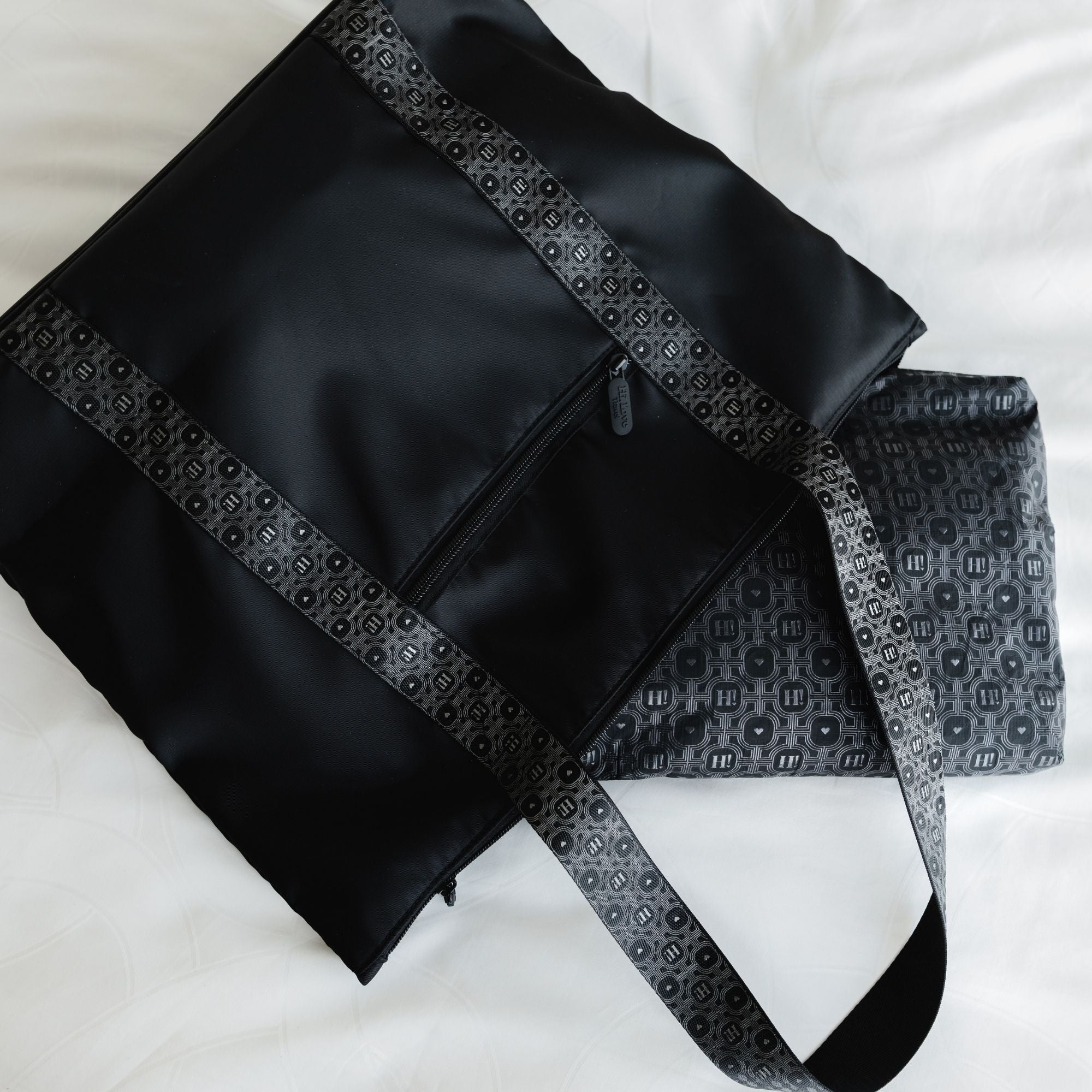 Close-up of the black signature tote's striped strap laid flat beside the matching signature patterned pouch.