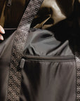 Close-up of the black tote's front zip pocket beside the signature striped strap.