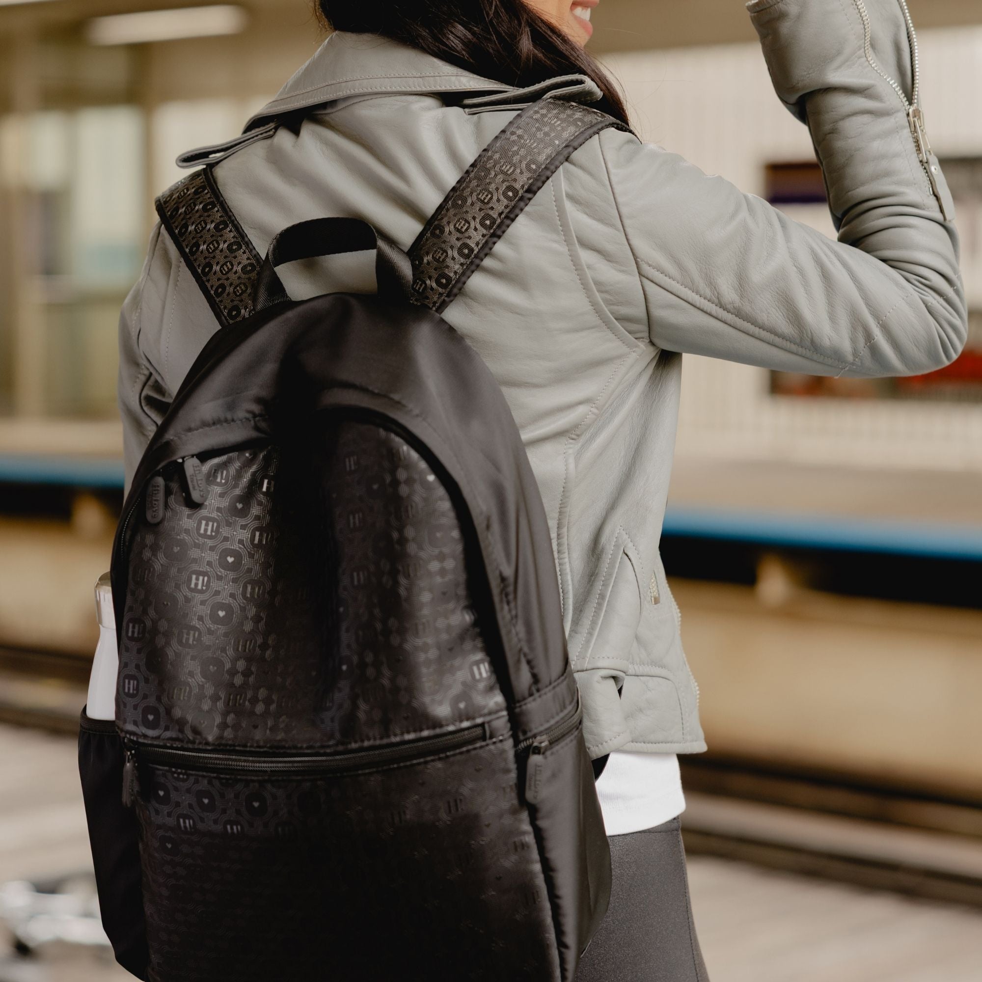 Woman walking through a train station wearing the black signature backpack on her shoulders.