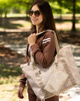 Woman smiling outdoors holding signature travel tote in beige