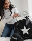 Woman smiling while packing a black Signature Weekender with a silver star and holding a silver medium Pouch with a black star.