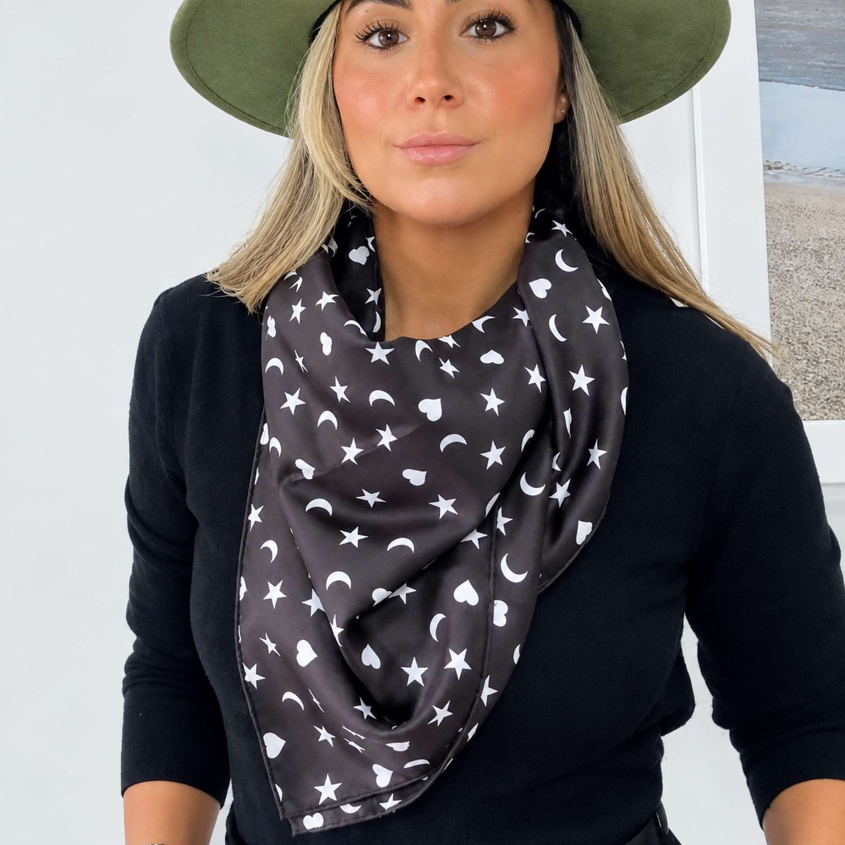 Model wearing the black Signature scarf with white hearts, moons and stars draped loosely around her neck over black.