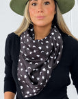 Model wearing the black Signature scarf with white hearts, moons and stars draped loosely around her neck over black.
