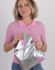 Woman holding two silver pouches with pink lips against a plain background