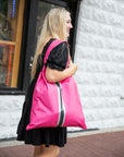 Young woman walking outside a shop holding a hot pink tote bag over her shoulder