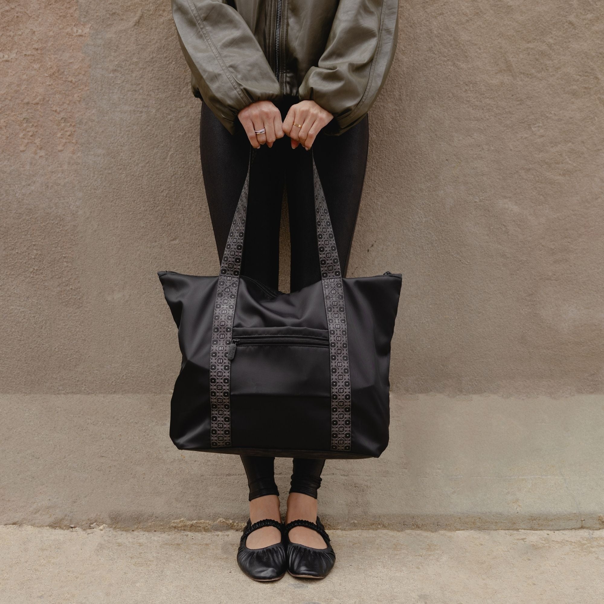 Woman standing on a stoop holding the black signature tote by its straps in front of her.