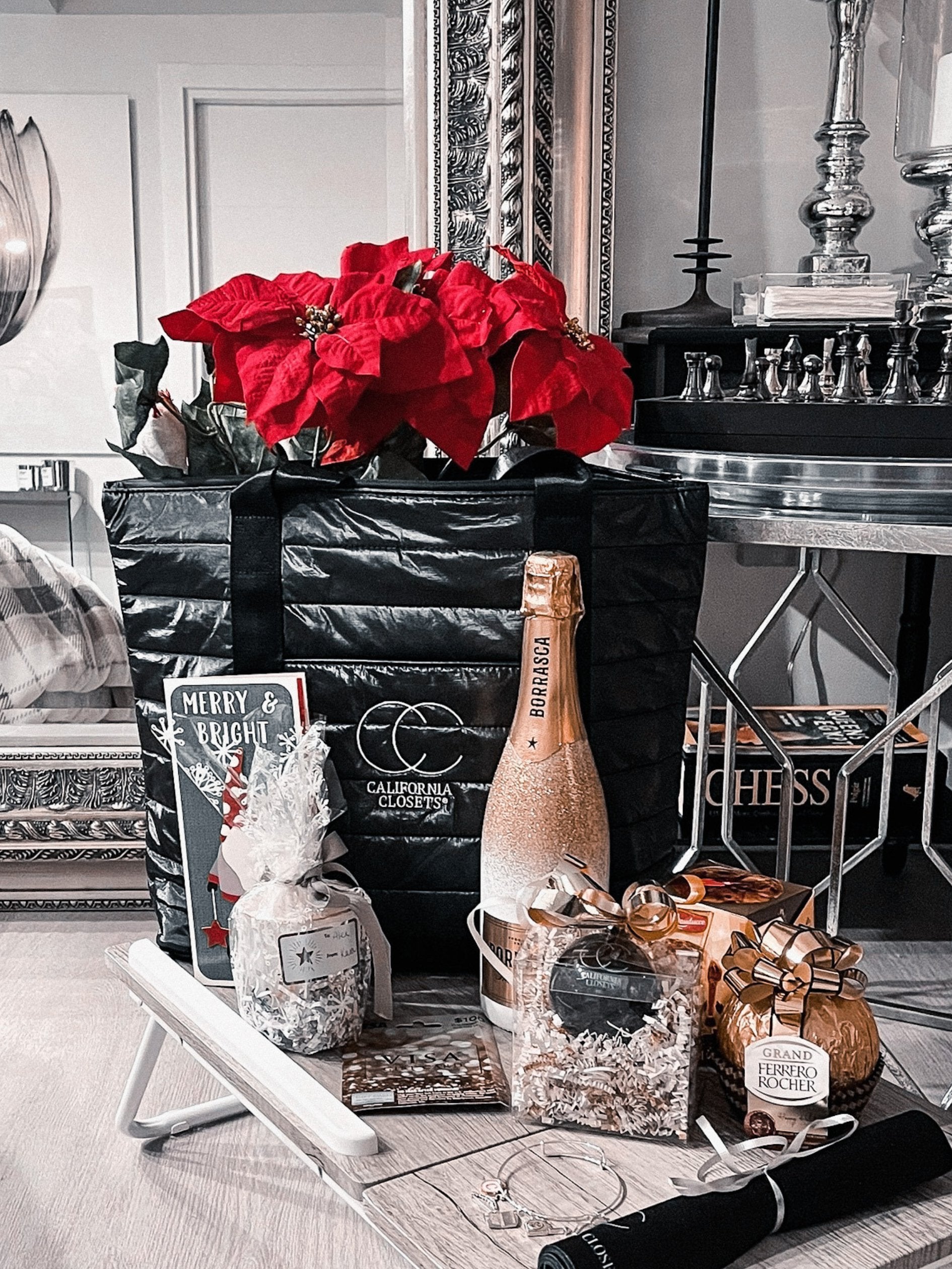 Decorative table setting with champagne, flowers, a custom embroidered shimmer black tote and books in a stylish room.