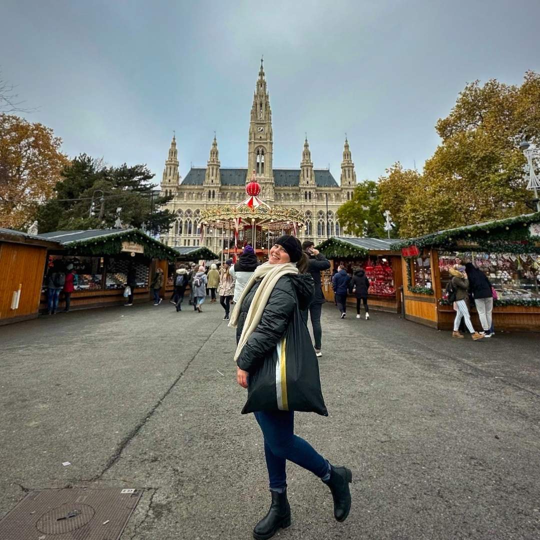 A person walking carrying a black stripe tote in a festive market in Vienna with a large ornate building in the background