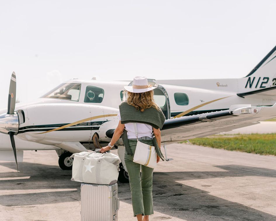 Woman with a suitcase standing in front of a small airplane on a runway.