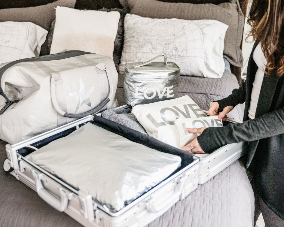 Person packing a suitcase with pouches and a weekender bag on the bed.