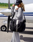 Traveler carrying the Signature Weekender in Pewter Silver by the shoulder strap next to a private airplane wearing a gray sweat suit.