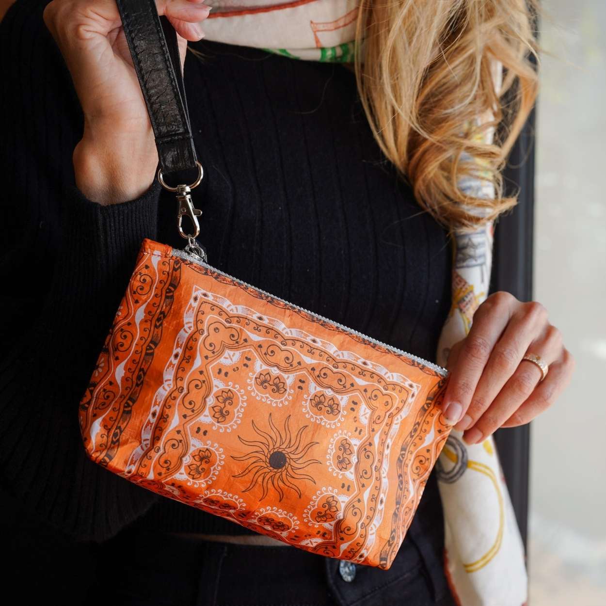 Person holding an orange bandana patterned wristlet bag