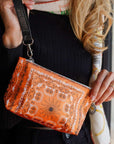 Person holding an orange bandana patterned wristlet bag