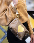 Woman wearing a bronze shimmer wristlet pouch with a gold heart design over her shoulder while overlooking a river in a fall landscape.