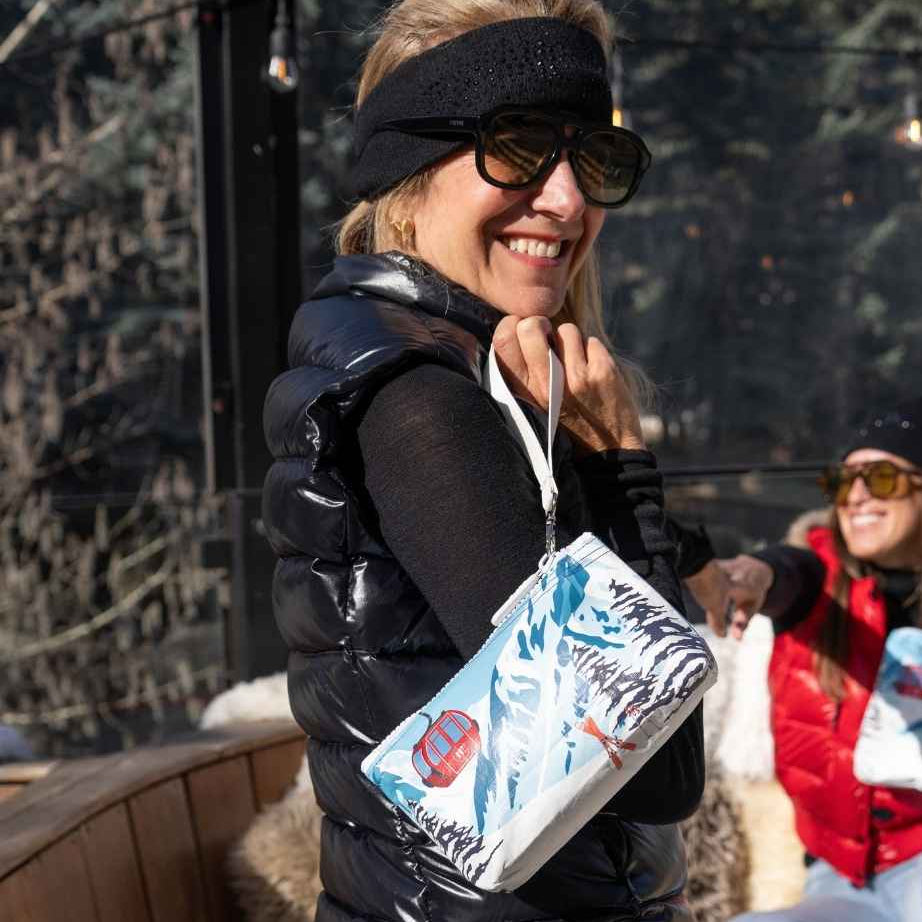 Two women holding hands and coordinating zipper pouches with a red gondola and snowy mountain print while relaxing at a ski resort.