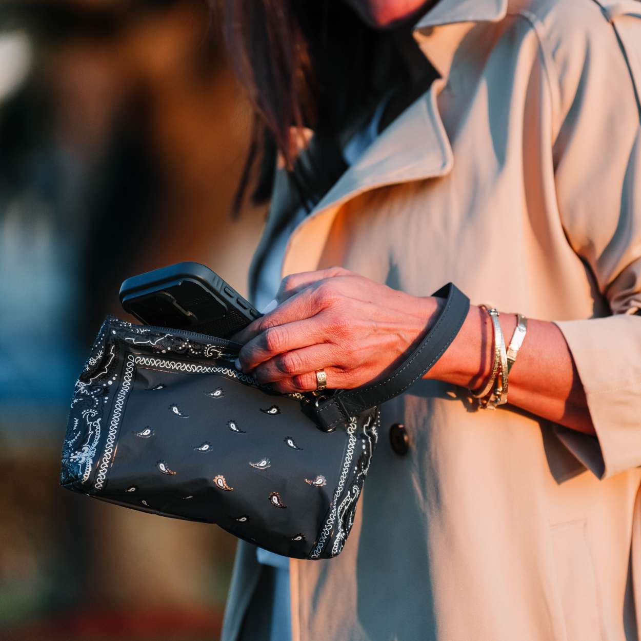 Person holding a navy blue wristlet with bandana patterns, wearing a beige coat.