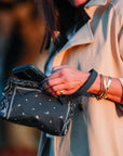 Person holding a navy blue wristlet with bandana patterns, wearing a beige coat.
