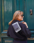 Woman with a black coat and bandana patterned bag standing in front of a green door.