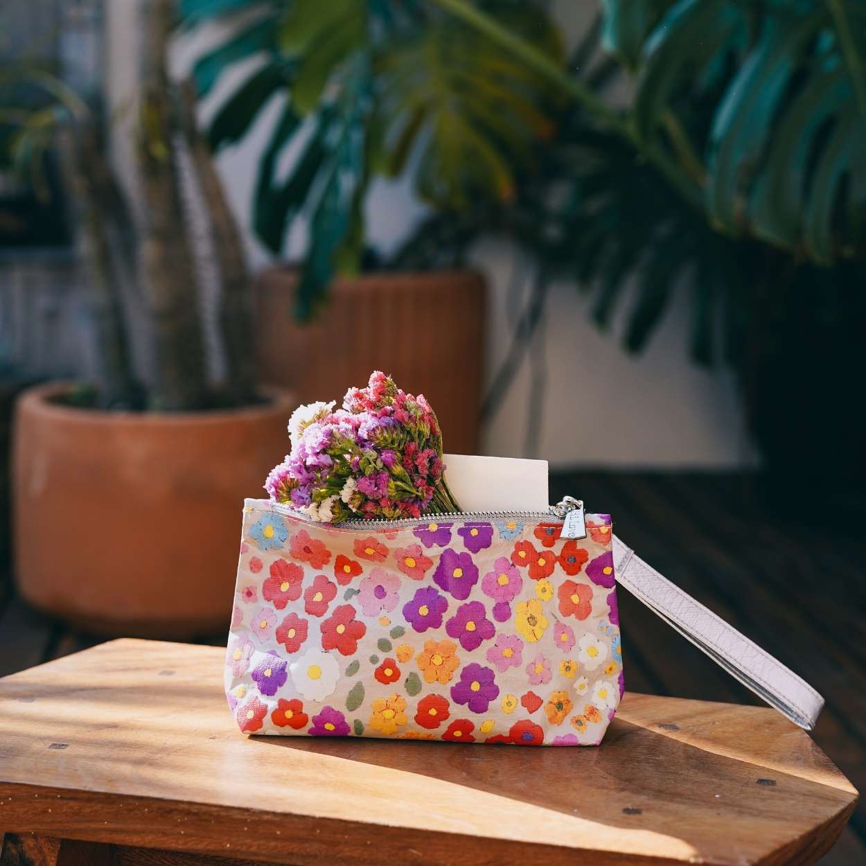 Floral-patterned wristlet with flowers and a candle on a wooden surface with plants in the background