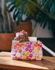 Floral-patterned wristlet with flowers and a candle on a wooden surface with plants in the background