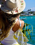 Woman wearing a sun hat and yellow heart wristlet with a scenic waterfront background