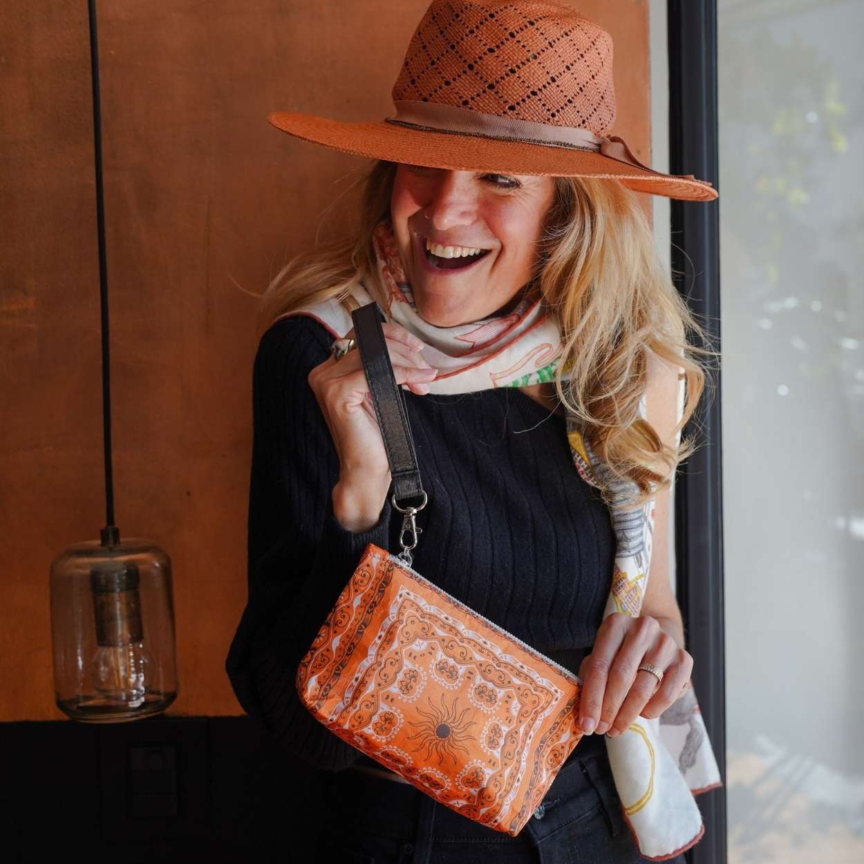 Woman wearing an orange hat and holding an orange bandana patterned bag indoors.