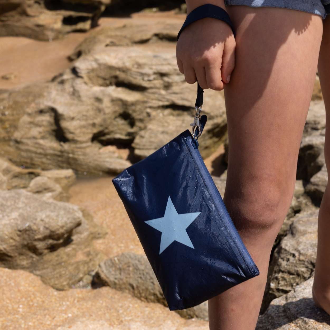 Girl on the beach holding a shimmer navy blue with light blue star wristlet bag.