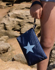 Girl on the beach holding a shimmer navy blue with light blue star wristlet bag.