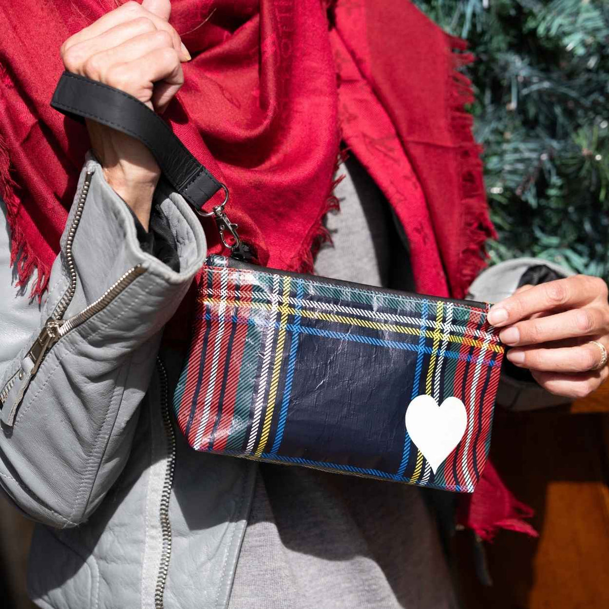 Hand holding zip wristlet in tartan plaid with red scarf and gray jacket in the background. 