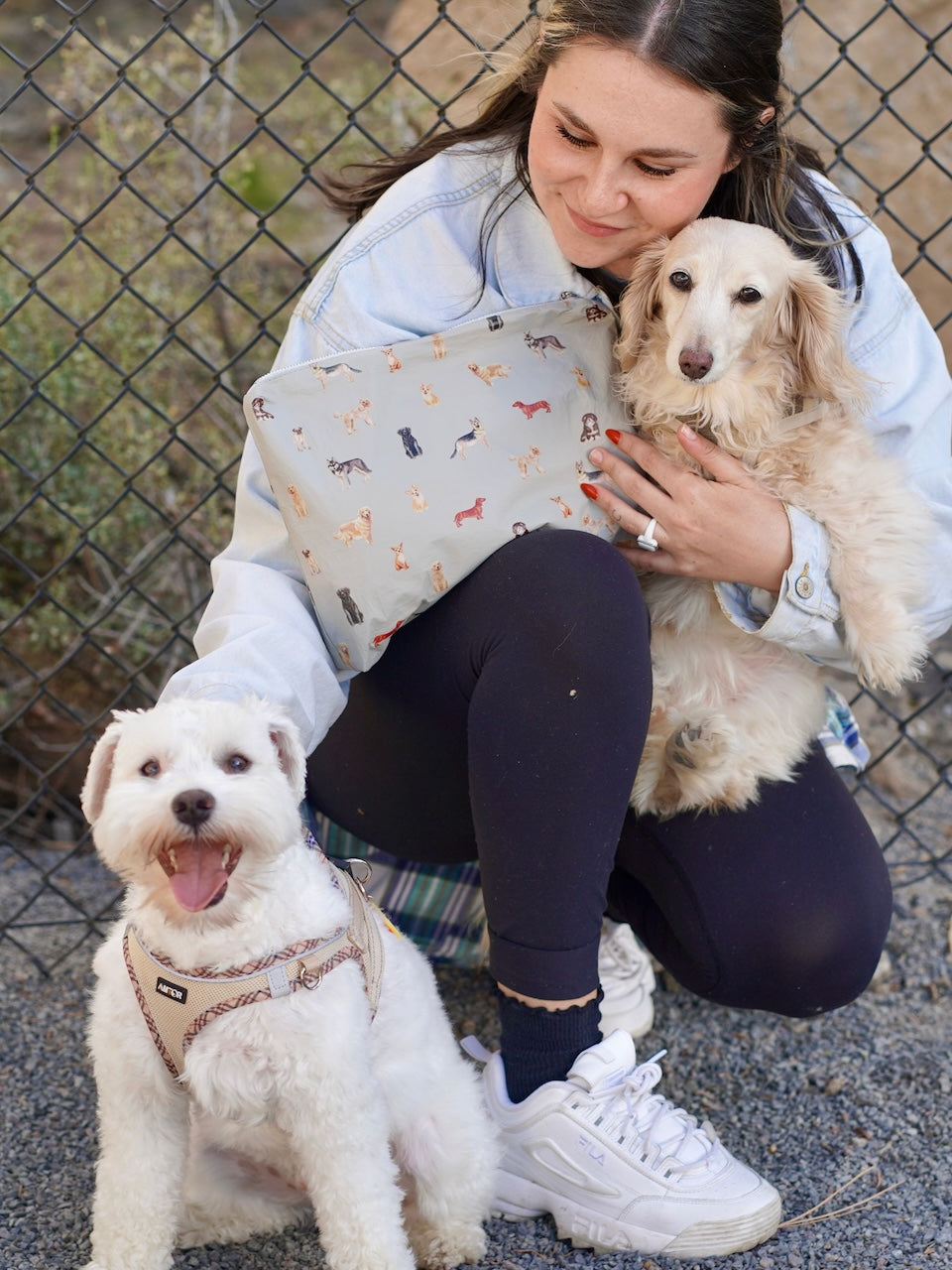 Woman holding a dog and sitting next to another dog on a leash, with a zipper pouch with dog print.