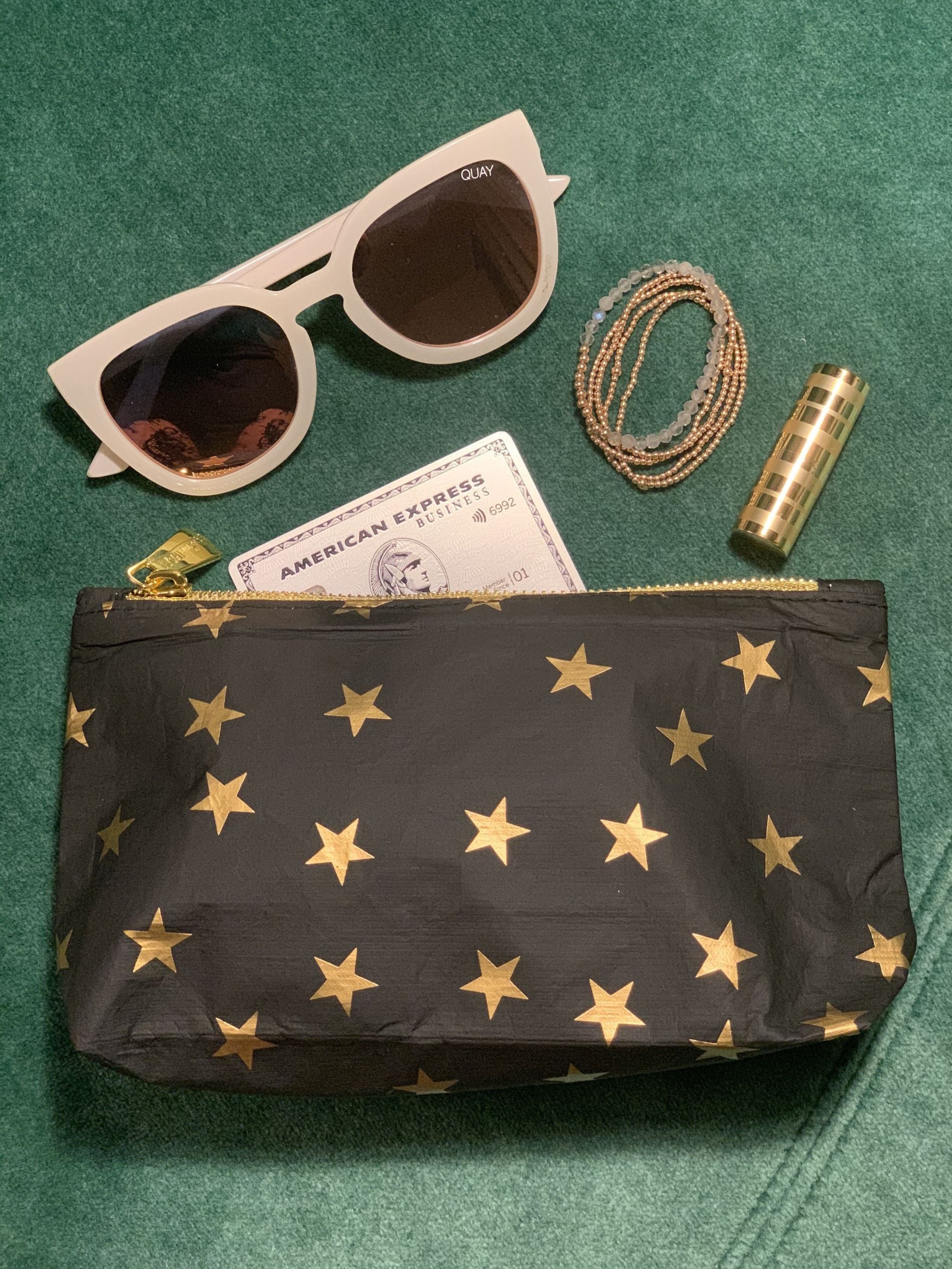 Versatile mini zipper pouch in black with myriad of gold stars on green background
