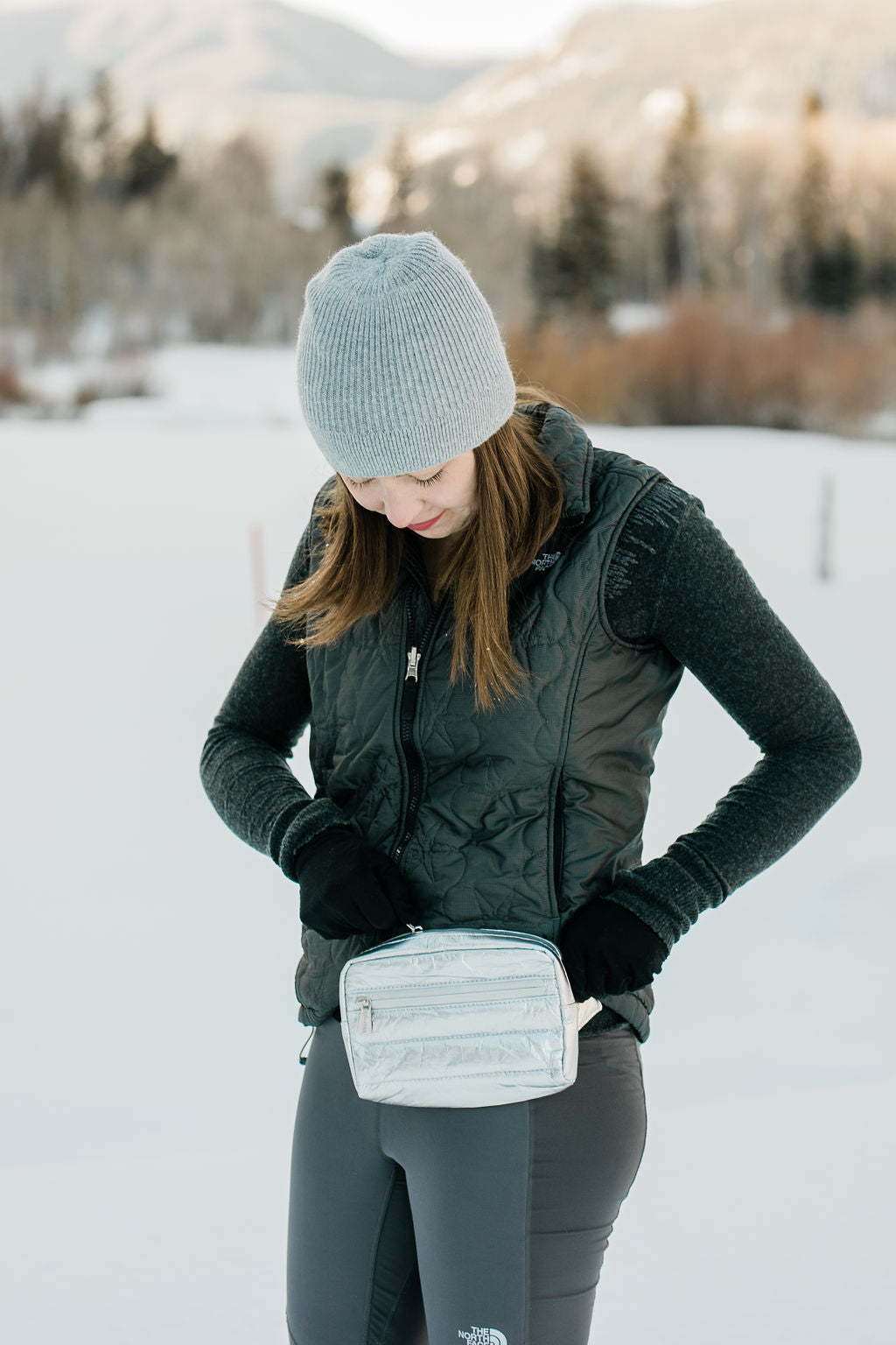 Woman in snow wearing Puffer Crossbody Fanny Pack Belt Bag in Silver with Black Strap