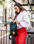 Woman taking a water bottle out of the black puffer crossbody backpack with gold heart outdoors