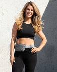 Woman standing against wall wearing Layflat Fanny Pack Belt Bag in Cool Gray