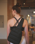 Woman in activewear wearing the black puffer crossbody backpack inside a fitness studio