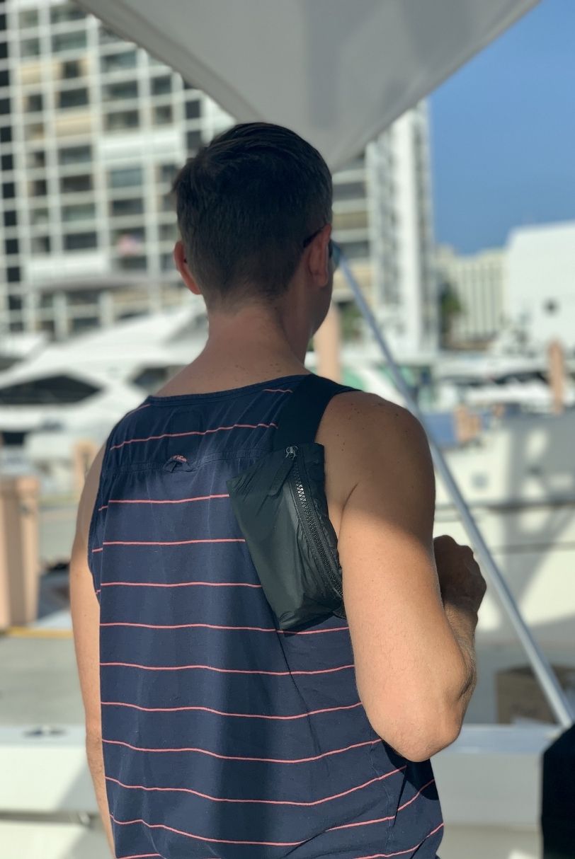 Lay Flat belt bag in black worn over the shoulder by a man on a boat.