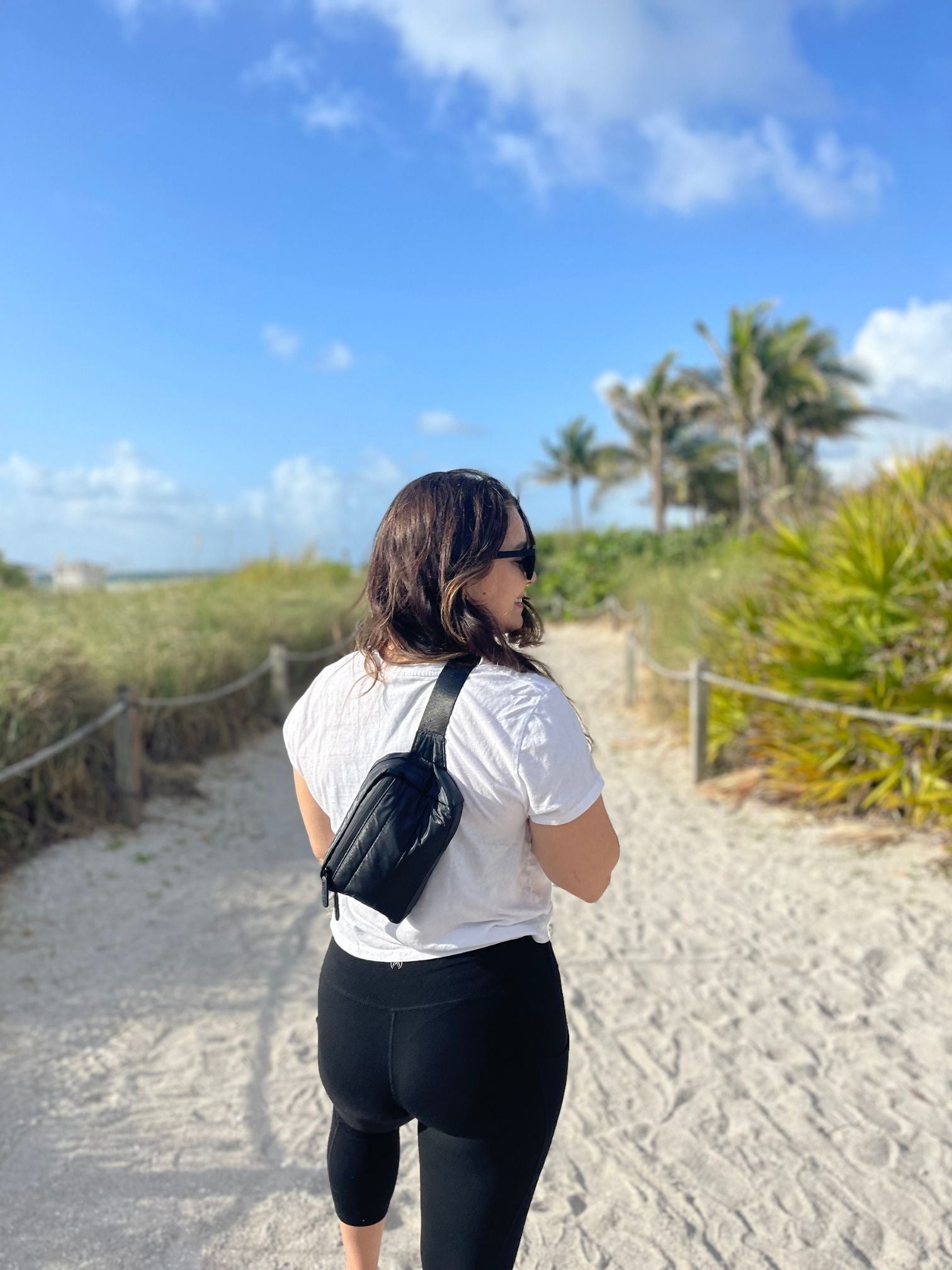 Woman on beach wearing Puffer Crossbody Fanny Pack Belt Bag in Shimmer Black