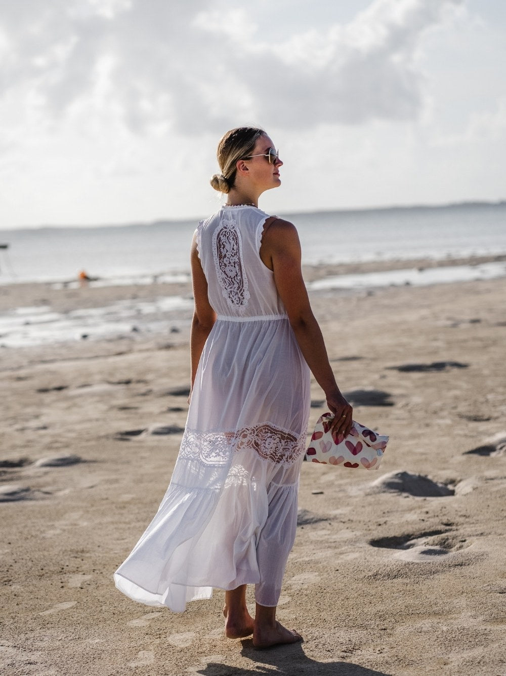 Woman on beach wearing white dress and medium zipper pouch in "language of love" heart print