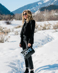 Woman in a black outfit and boots walking through snow, carrying the Medium Pouch in Black with Silver LOVE