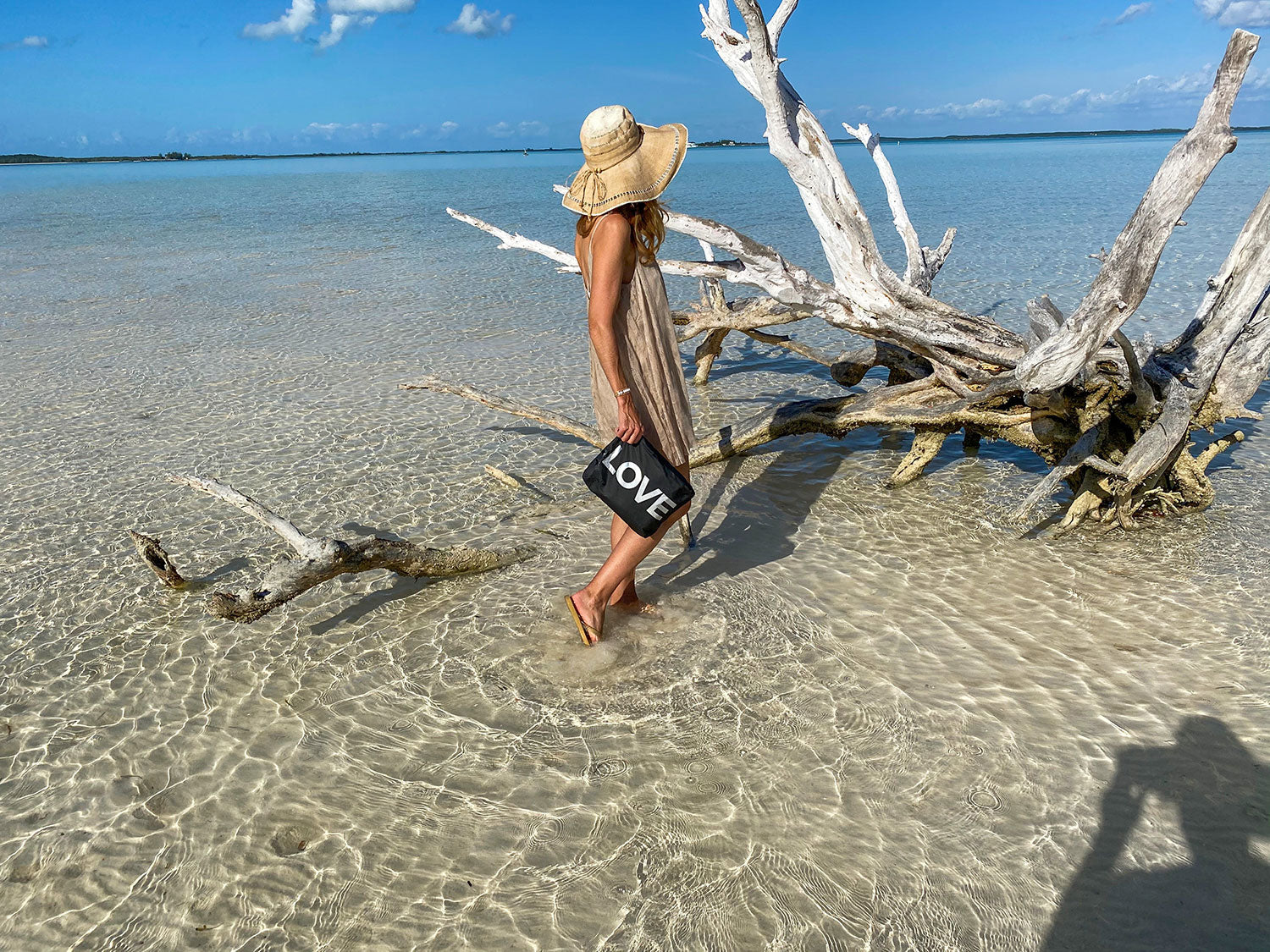 Women walking in shallow water by tree with a zipper pouch in black with silver love printed on it.